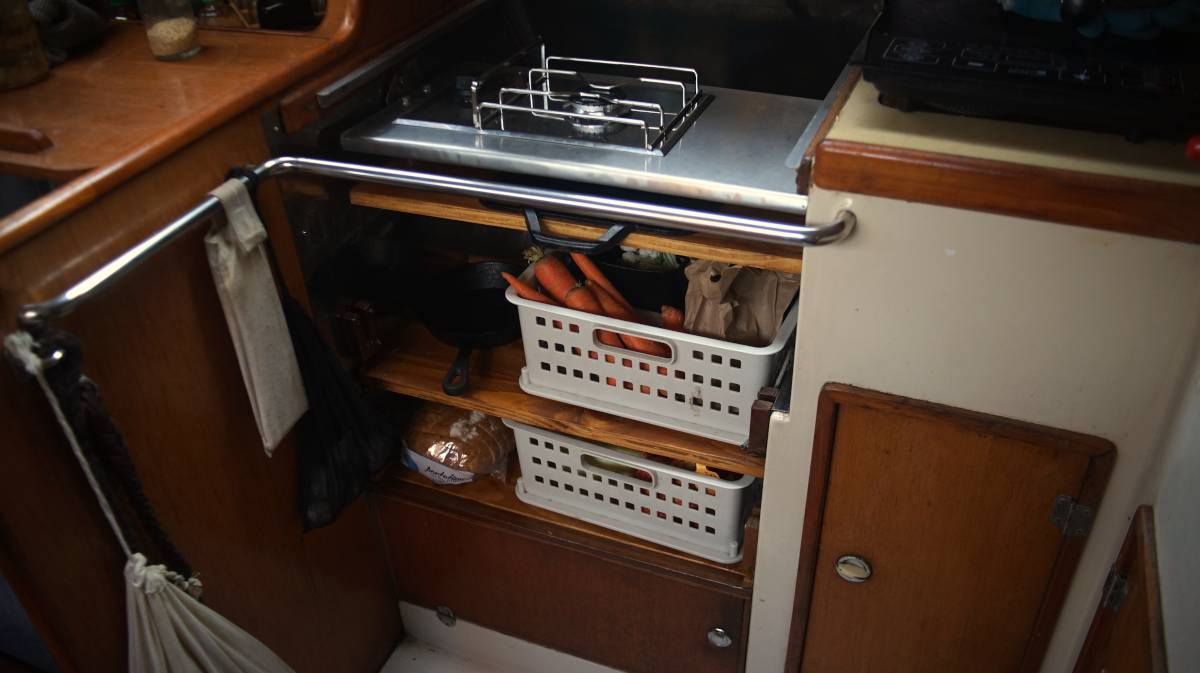 a view of Pino’s new galley setup with a single lpg gimballed burner layer over two shelves containing baskets of fresh produce