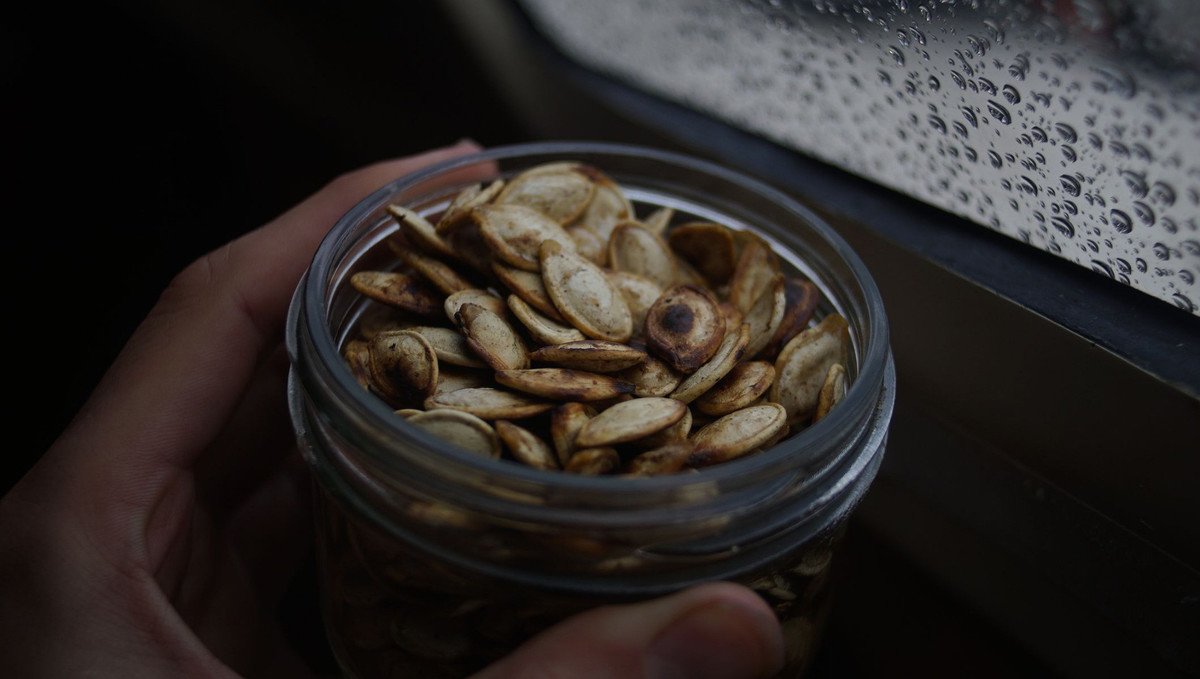 roasted pumpkin seed snack a photo of a hand holding a jar of roasted and salted pumpkin seeds with their shell