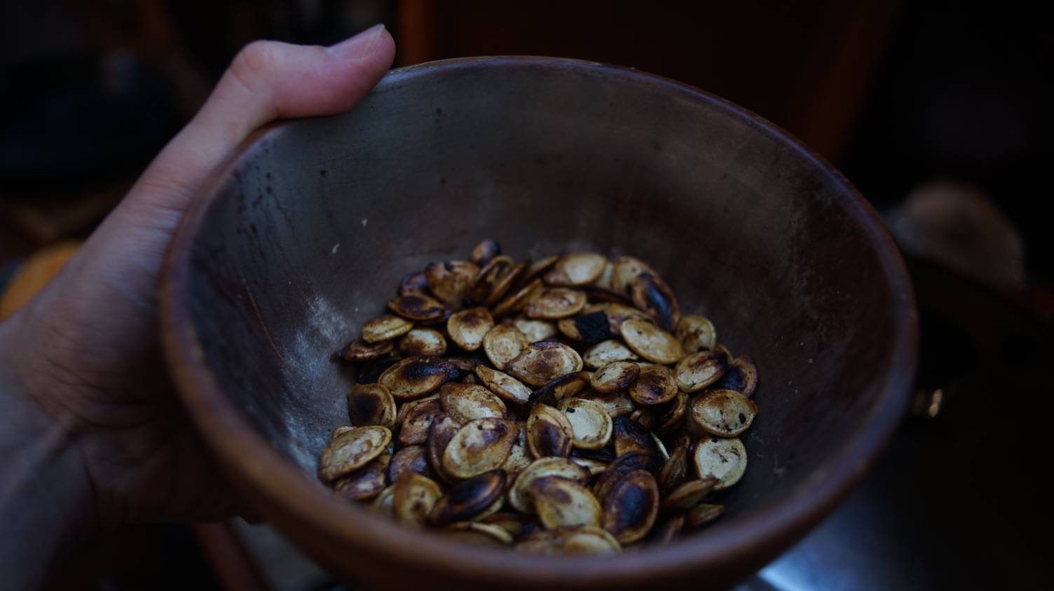 Uxn pumpkin A photo of a hand holding a bowl of roasted pumpkin seeds