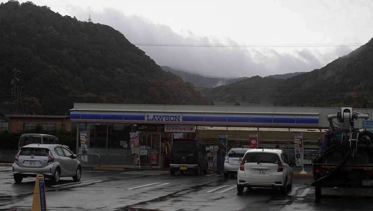 lawson shop in downtown Gokasho a photo of a small convenience store in rural japan, with fog and mountains in the background