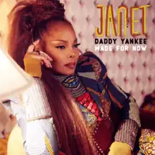 Janet Jackson in a colorful dress sitting in a thinking pose beside a table lamp