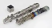 Tungsten rods with evaporated crystals, partially oxidized with colorful tarnish, and a 1&nbsp;cm3 tungsten cube for comparison