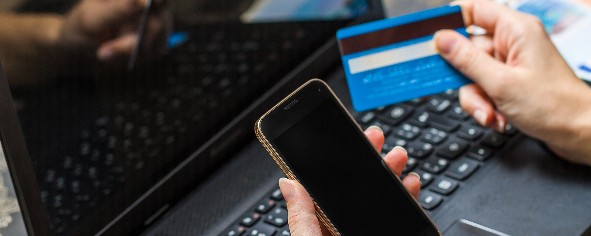 Las manos de un hombre sosteniendo una tarjeta de crédito y un teléfono móvil con una computadora portátil